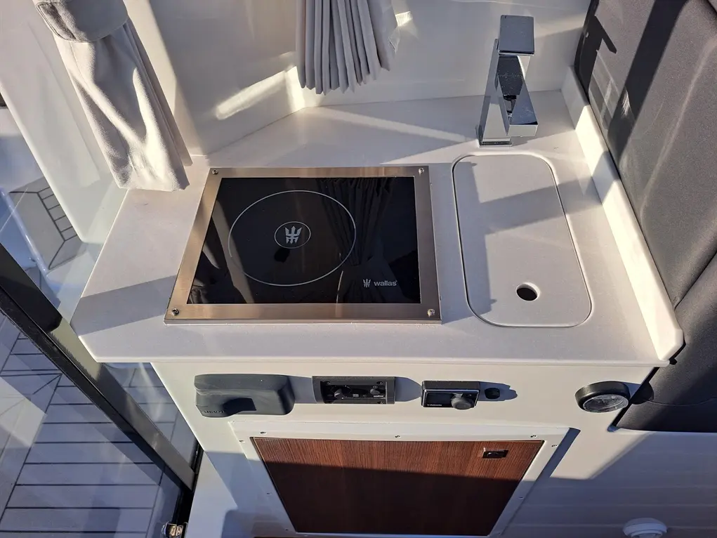 A modern boat kitchen countertop with an induction stove, faucet, and control panel, featuring a wood cabinet below.